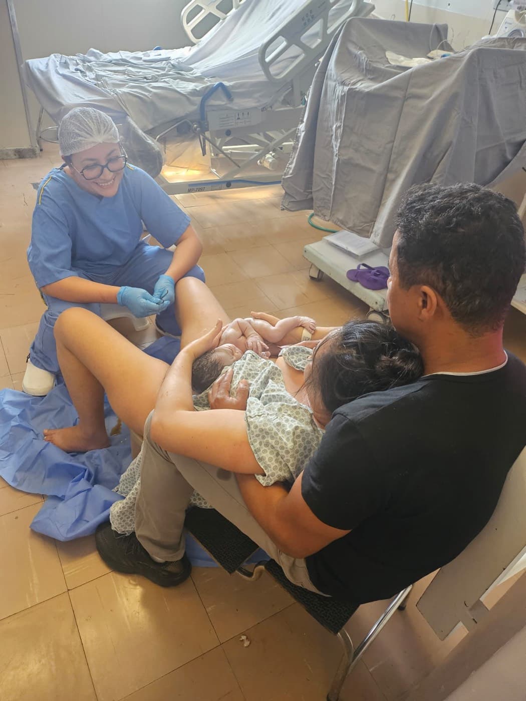 Mãe e bebê pele a pele logo após o nascimento, com o pai ao lado e Chayene assistindo